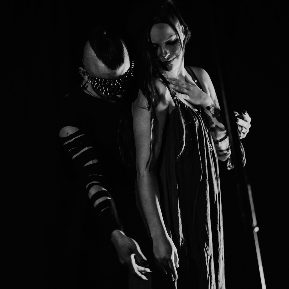 Two people in dark clothing perform an artistic dance movement together in low lighting conditions.