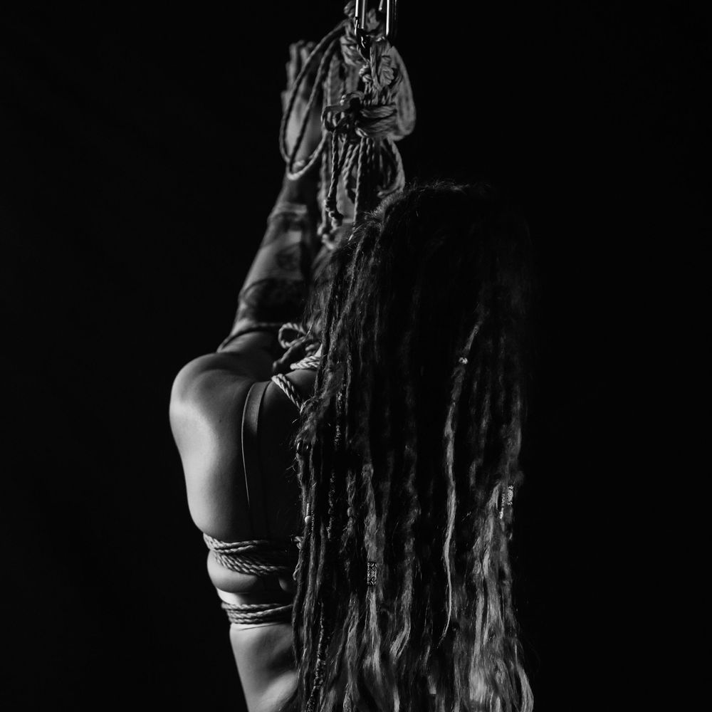 Black and white artistic photo series showing silhouette of person with dreadlocks in dramatic poses against dark backdrop.