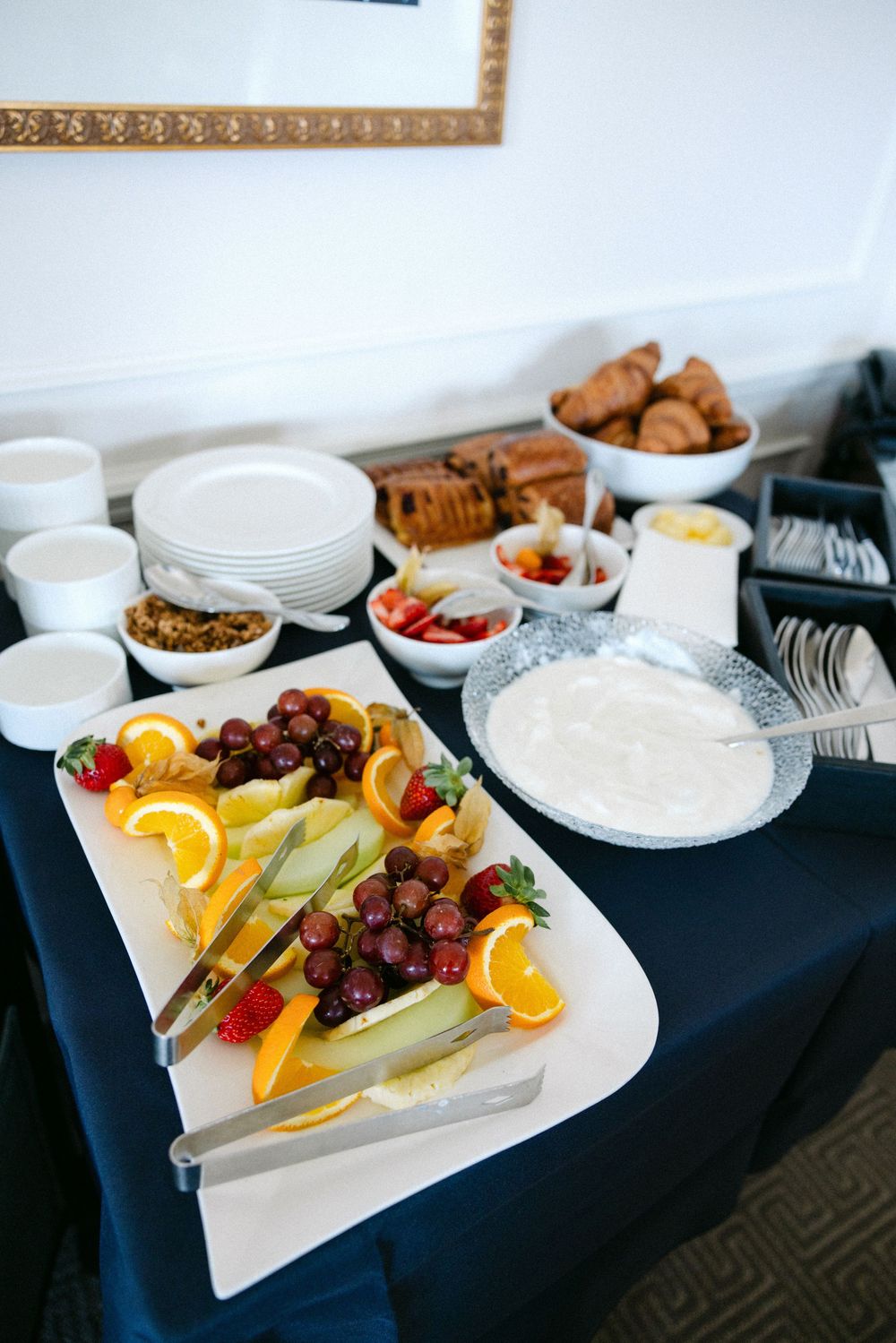 Fresh fruit and snack platter display with oranges, grapes, berries and assorted dips on a white serving tray.