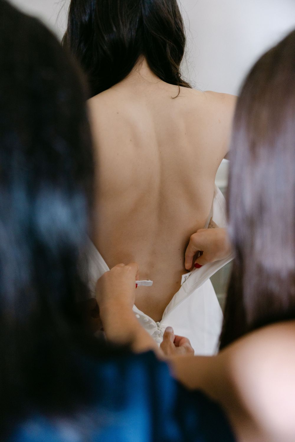 Close-up view of a woman's bare back during a bridal preparation showing meticulous dress lacing details.