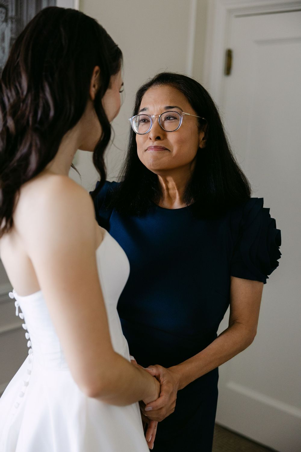 An emotional moment shared between a woman in a navy dress with puff sleeves and another in a white wedding gown.