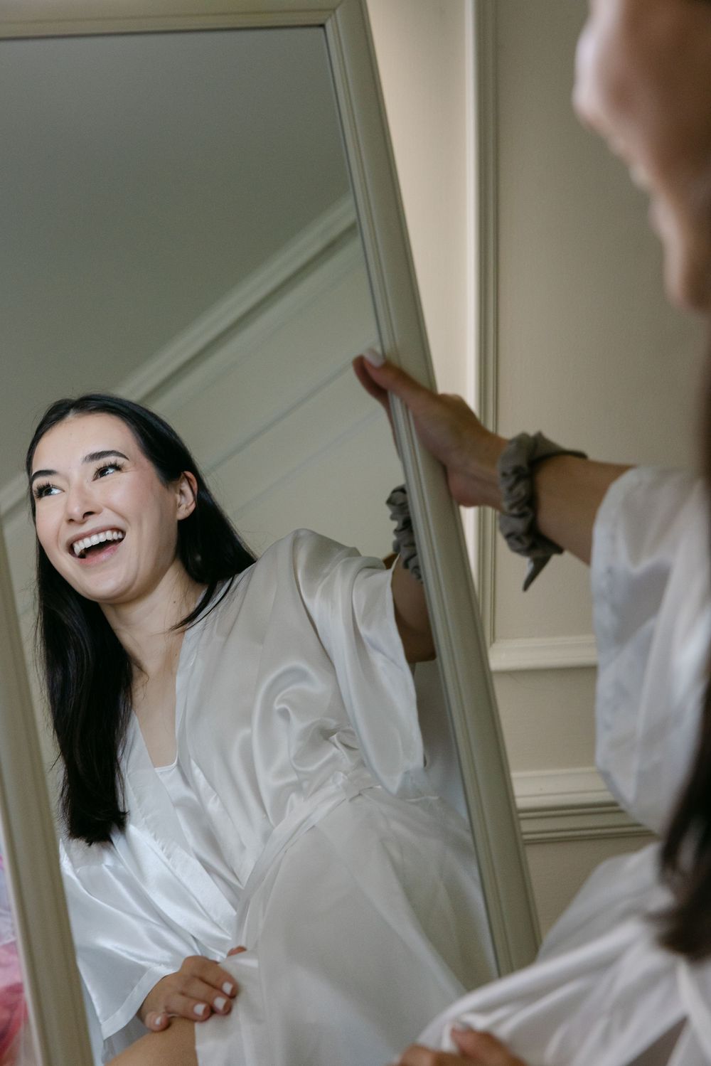 A person in a white shirt laughs joyfully while sitting in a bright interior space.