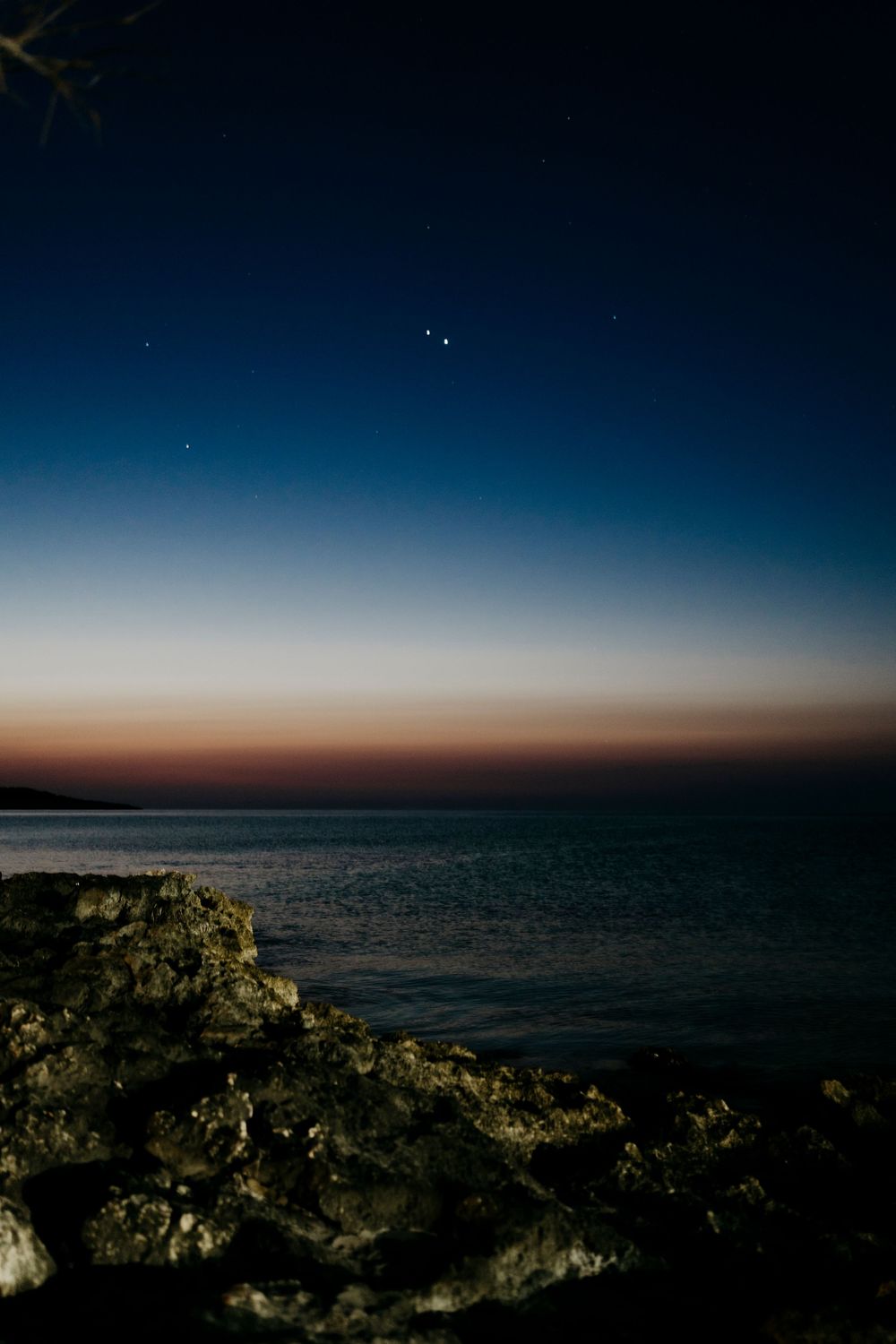 Panoramic twilight seascape with rocky coastline under deep blue sky.