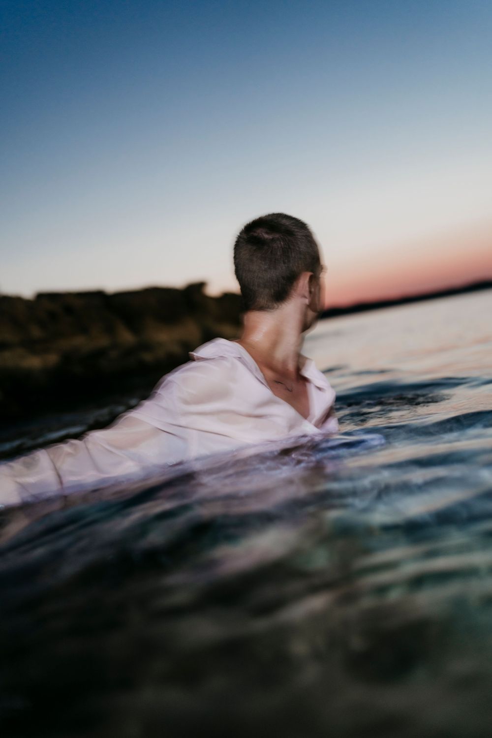 Person swimming in dark waters at sunset with dramatic shadows and reflections.