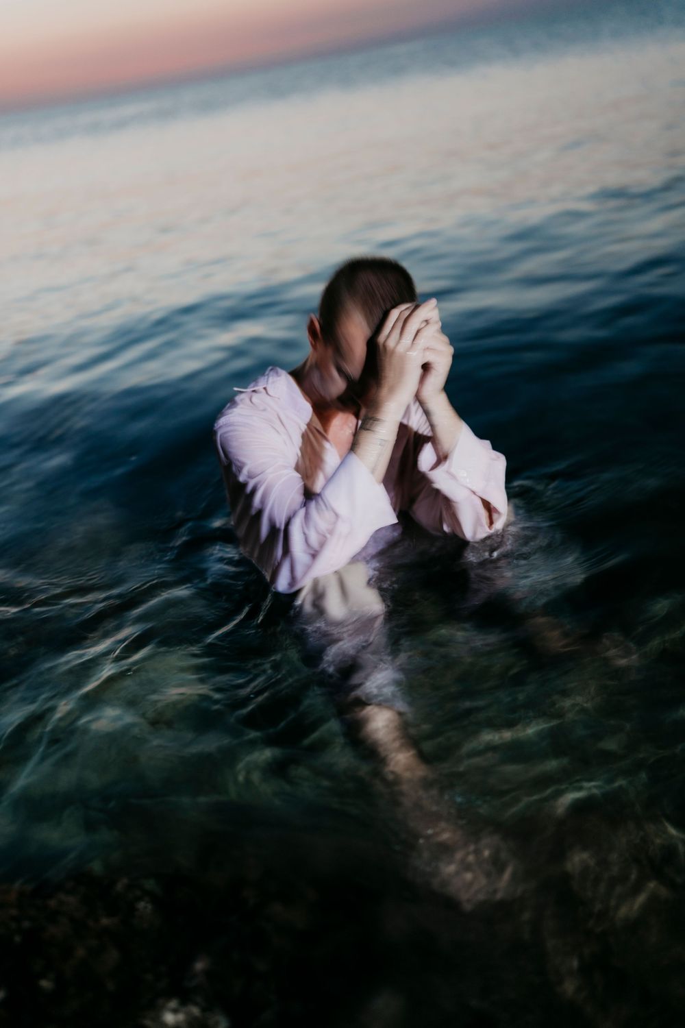 Figure in white submerged in ocean water during dusk.