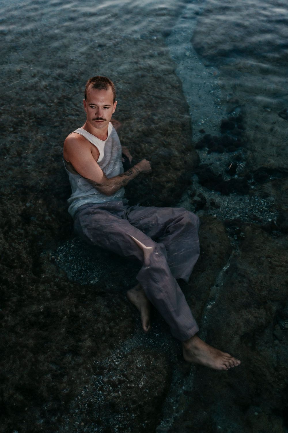 Figure in casual attire resting on wet rocks near the ocean.