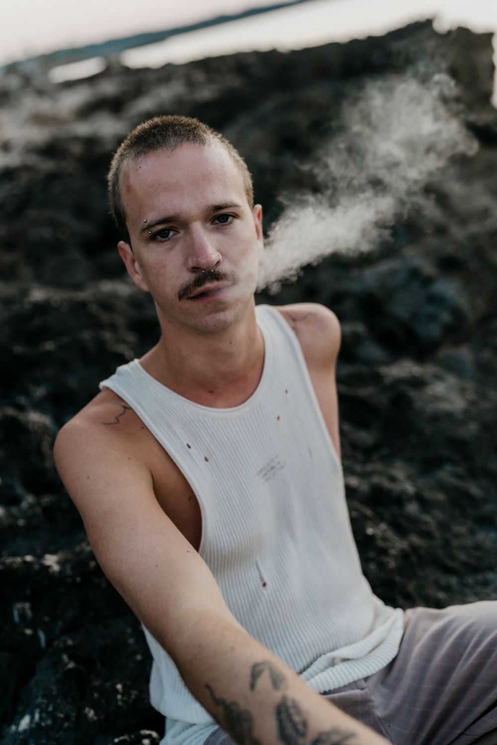 Person in white tank top posing on rocky coastal terrain during sunset.