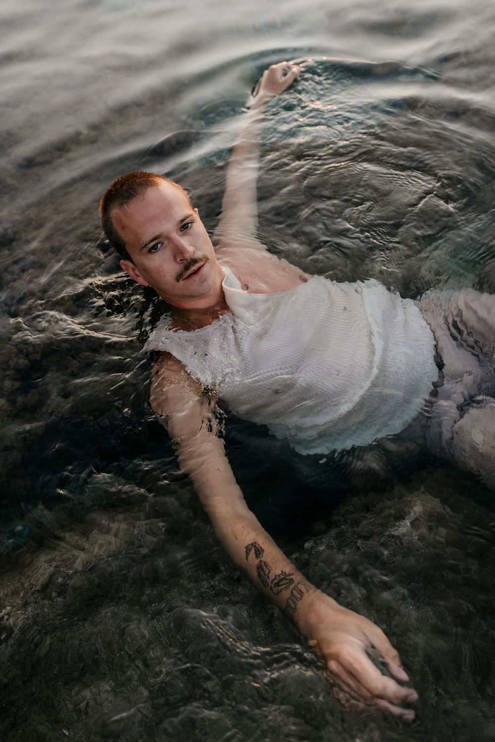 Figure in wet white clothing floating in dark rippling water.