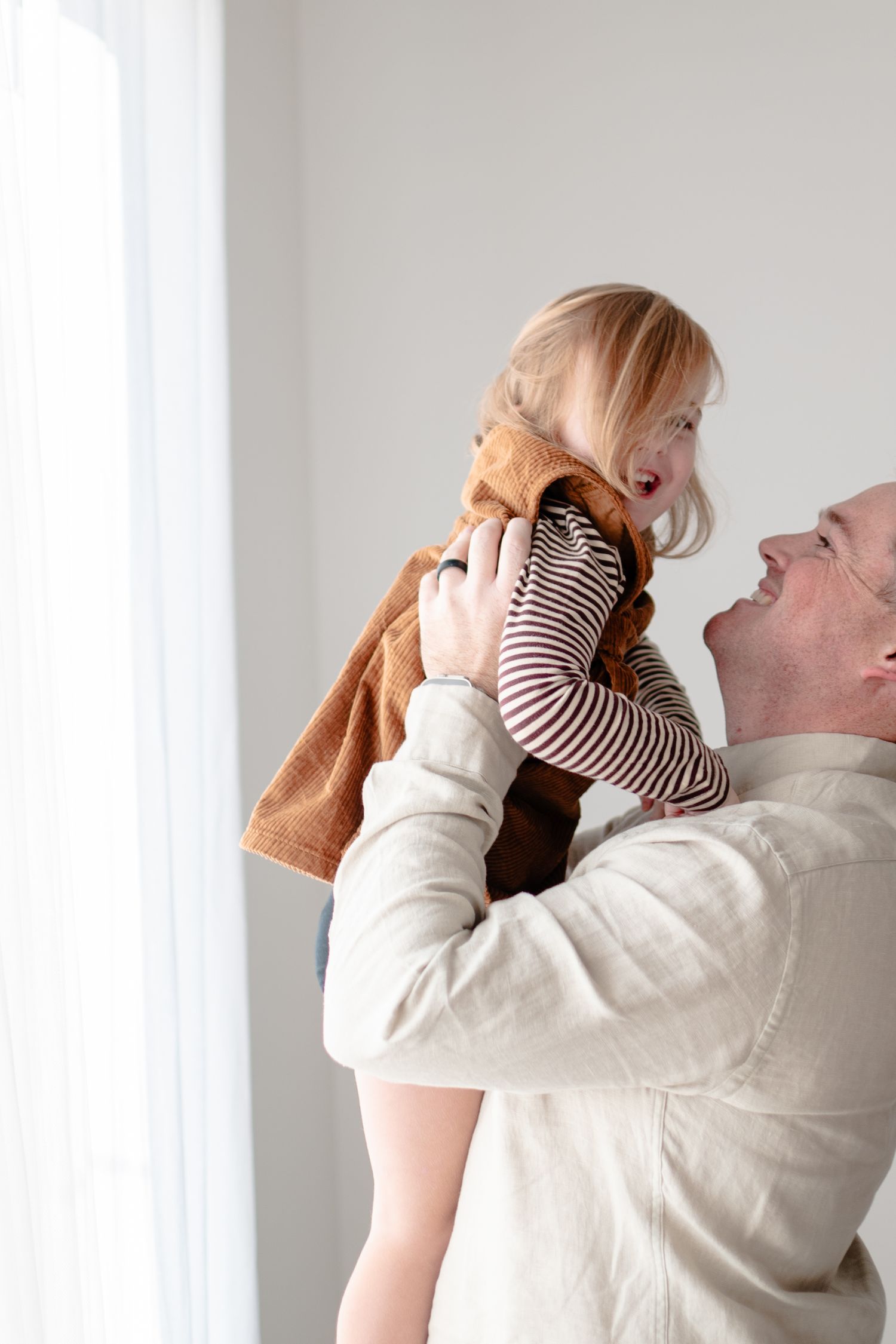 Four sequential photos show an adult holding and lifting a baby wearing a striped onesie against a white wall.