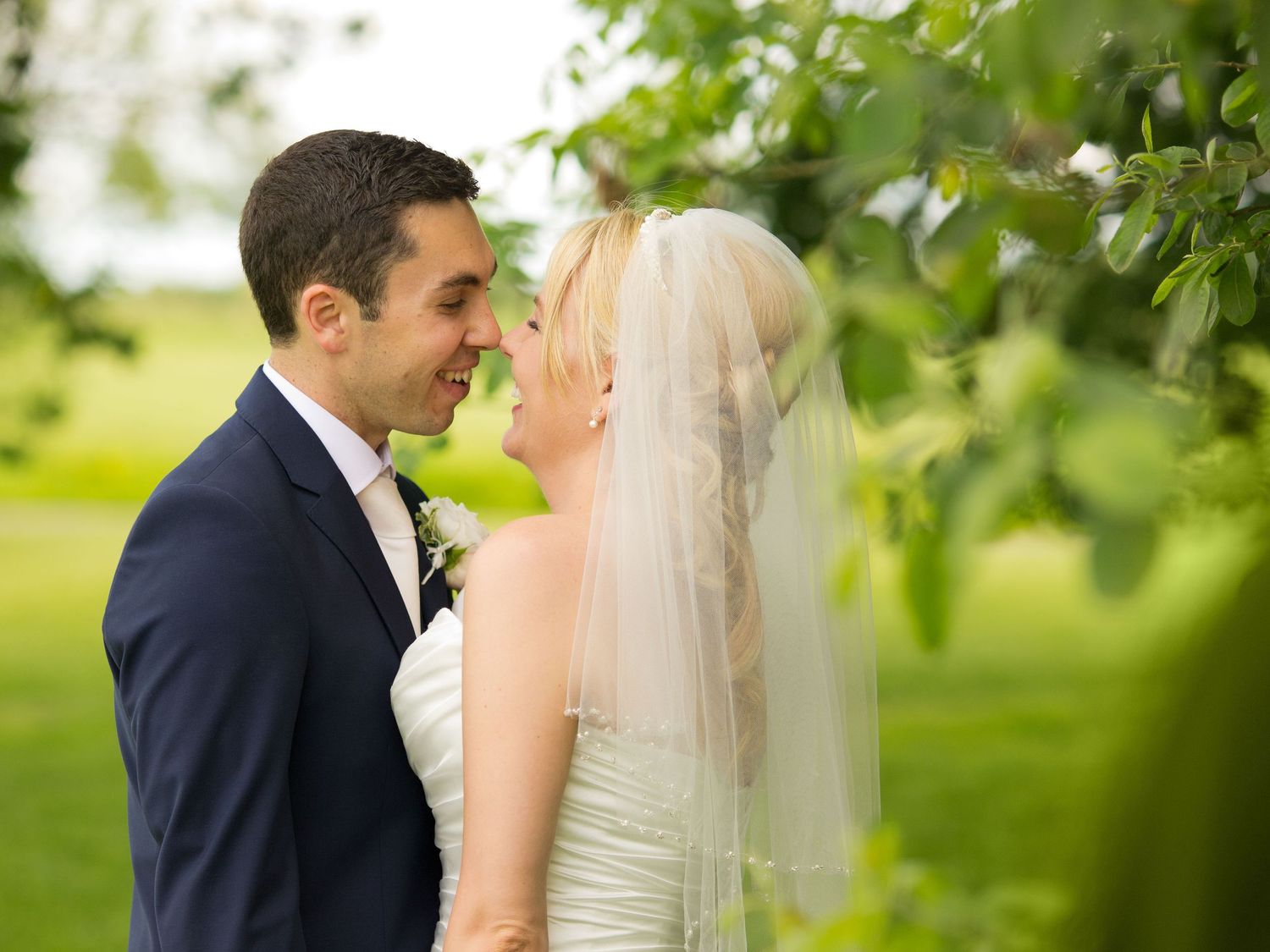 A couple shares intimate wedding moments under green foliage in outdoor garden photography.