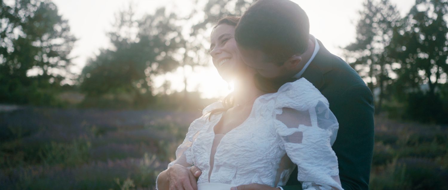 Couple embraces in romantic sunset moment with sunlight streaming through pine trees in the background.