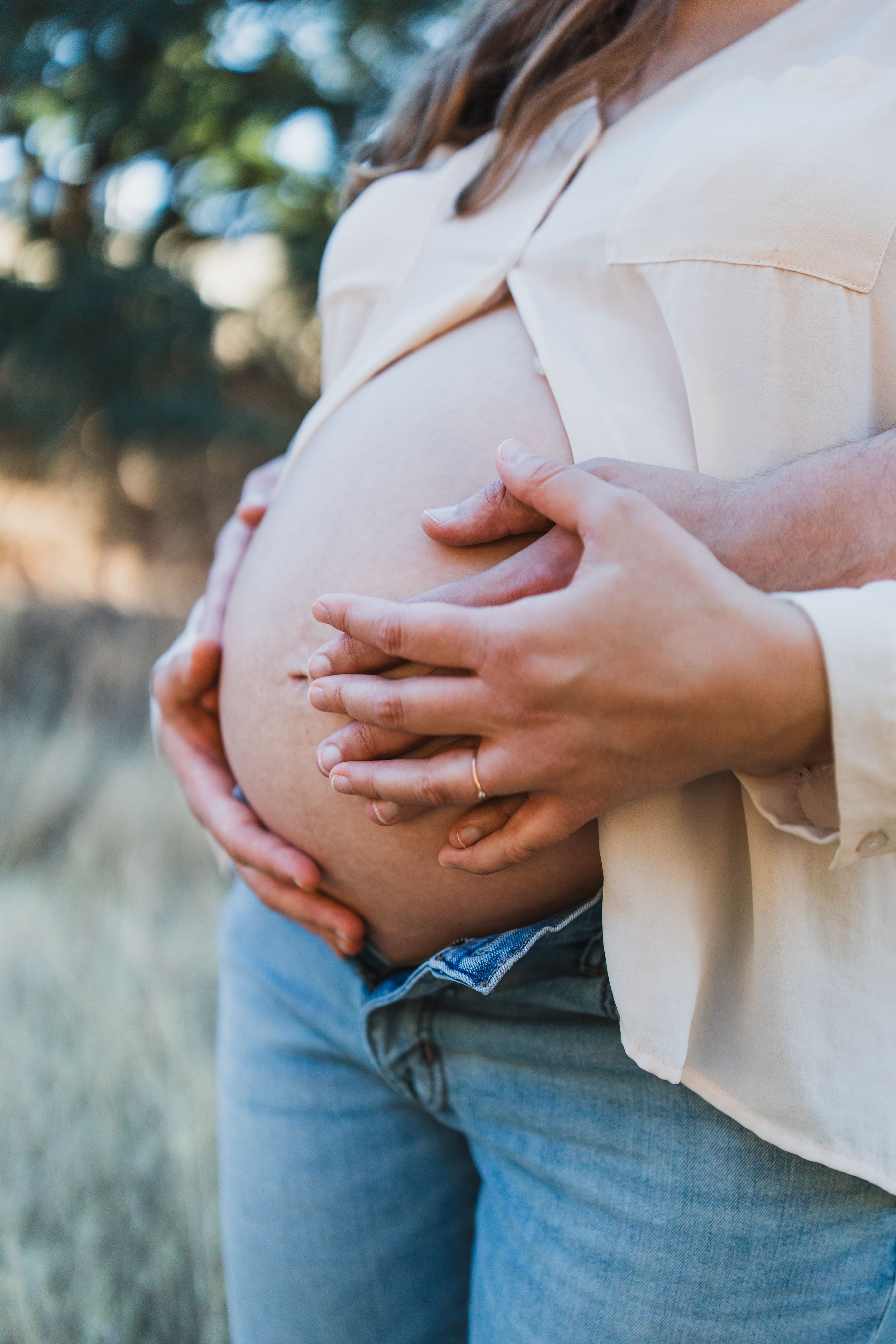 A close-up photo series showing hands cradling a pregnant belly while wearing jeans and a light pink blouse.