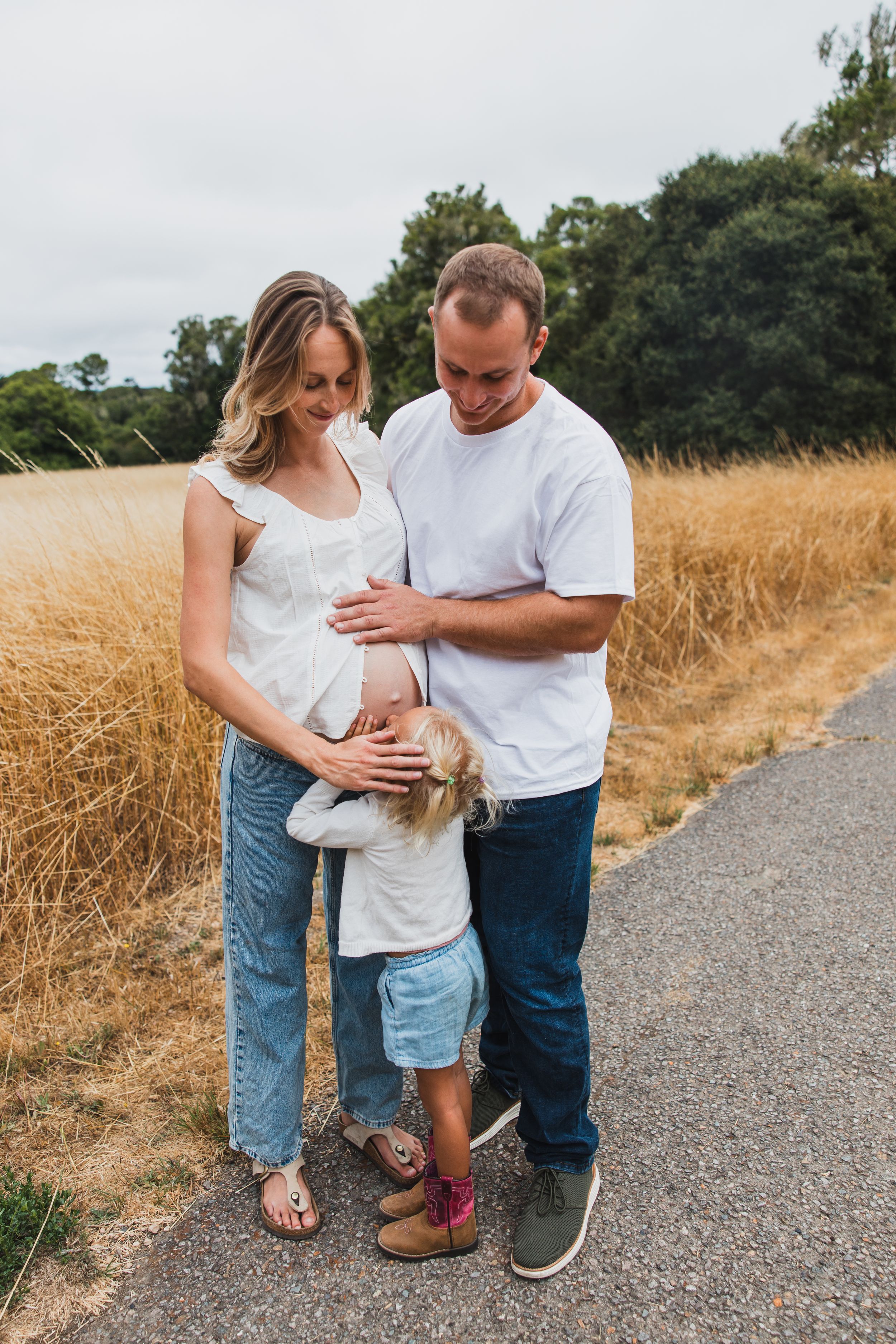 Family maternity photo session on path in golden summer field shows tender moments between expecting parents.