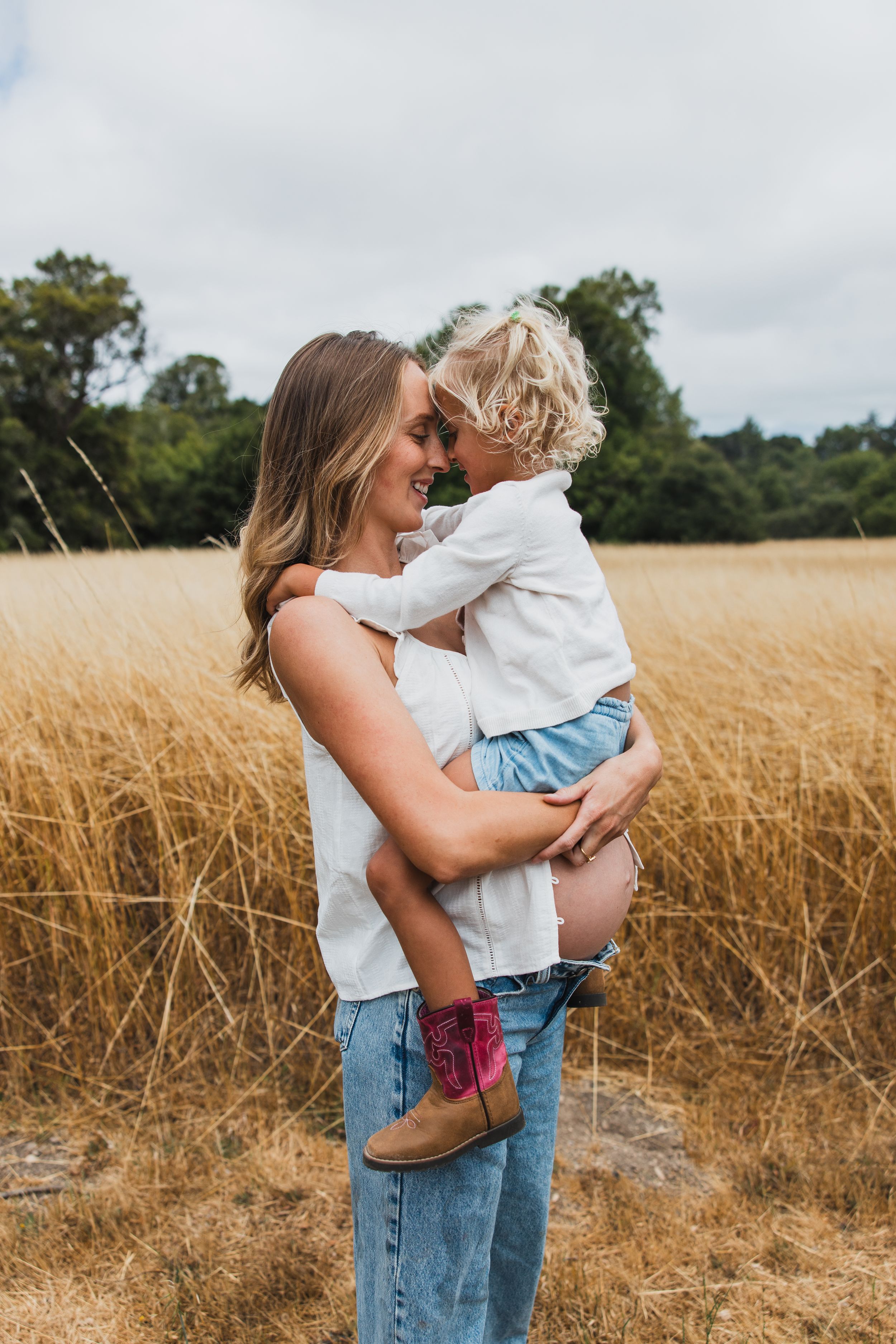 A loving embrace shared between mother and child in a golden wheat field on a cloudy summer day.
