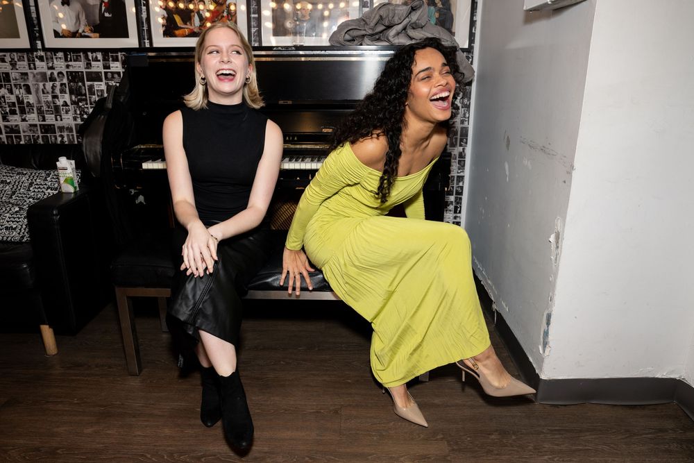 A person in a bright yellow dress and another in black dance energetically in what appears to be a studio space.