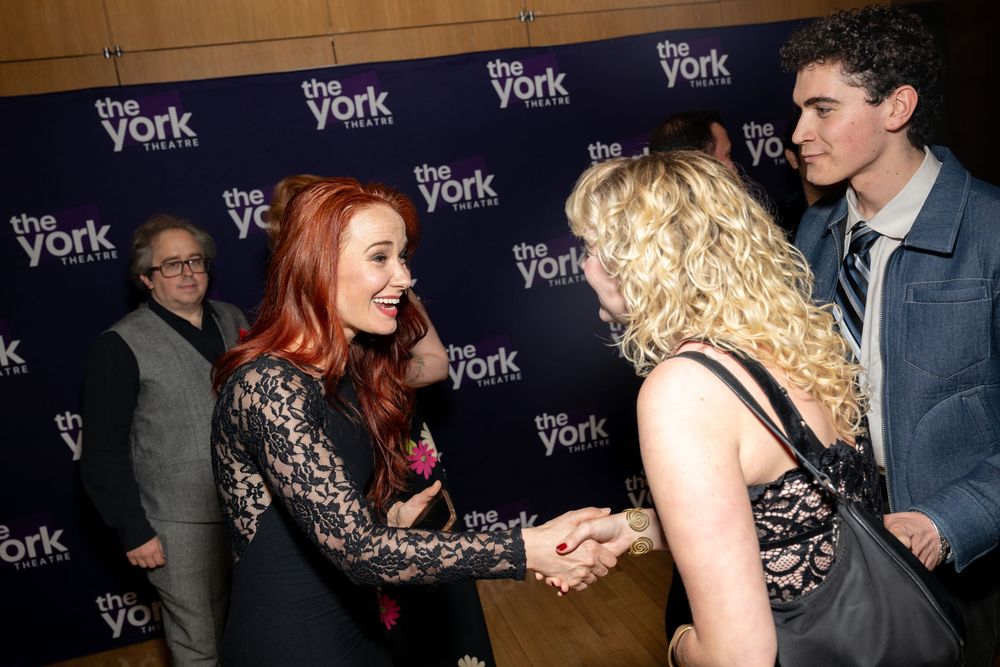 People greeting each other at The York Theatre event, with a red-haired woman shaking hands at a formal gathering.