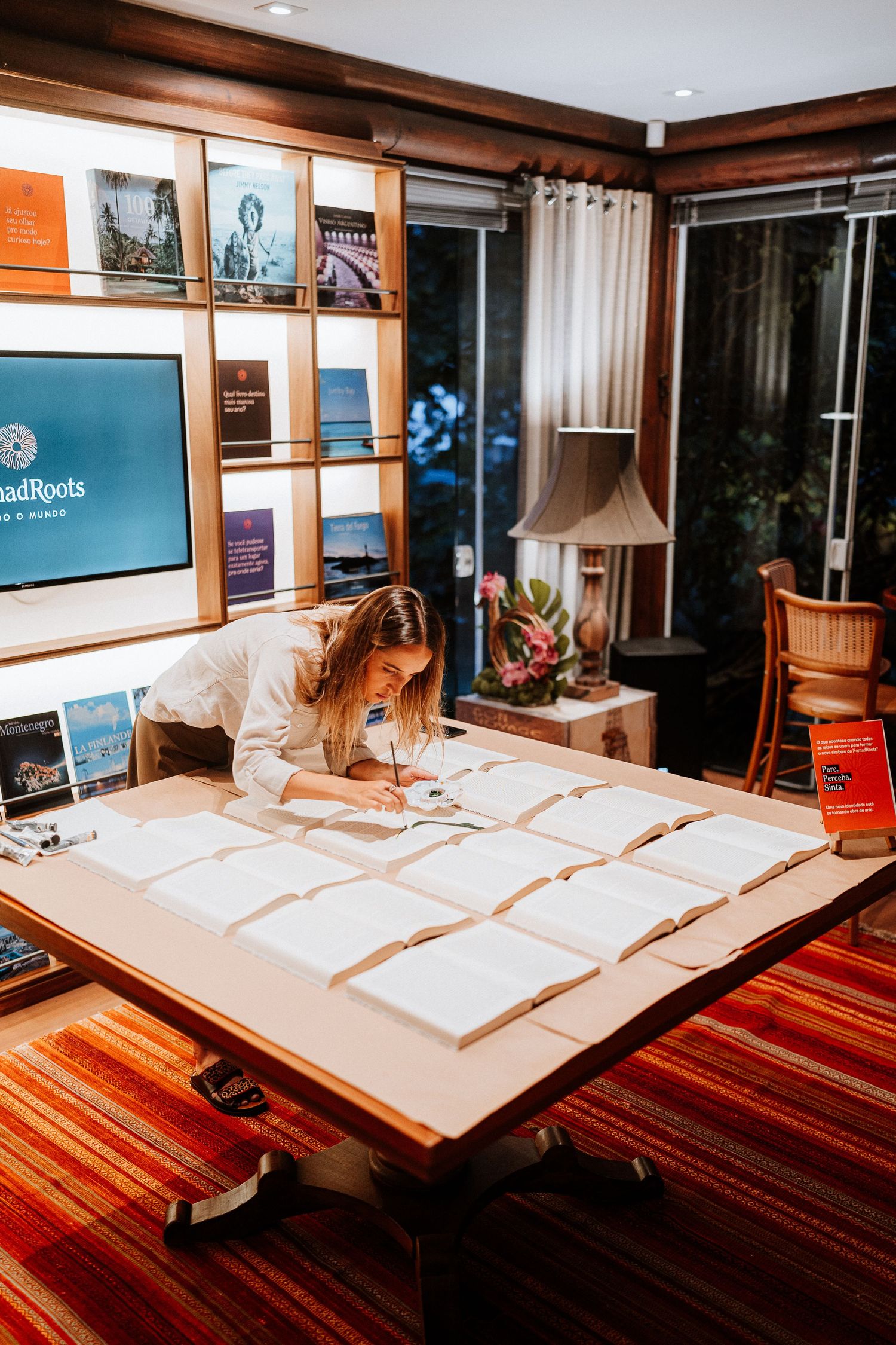 Person studying at desk with open books and documents laid out on wooden surface in warm lighting.