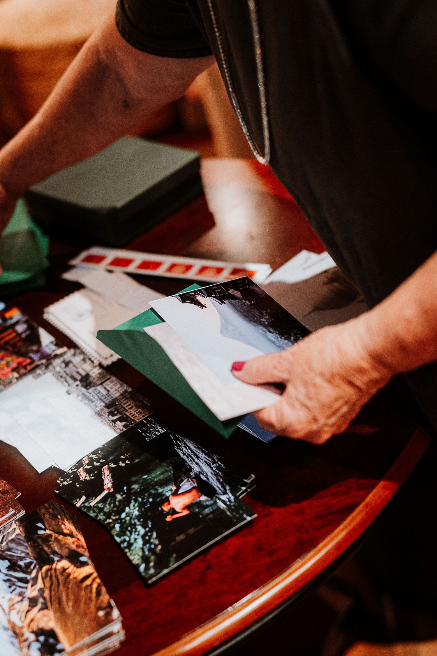 Hands sorting through photographs and documents on a wooden table.