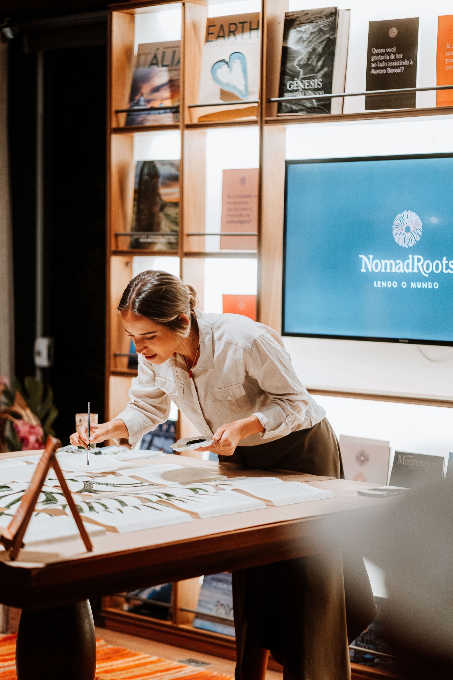 Person working at a desk with books displayed on shelves behind a Nomadpoet logo screen.
