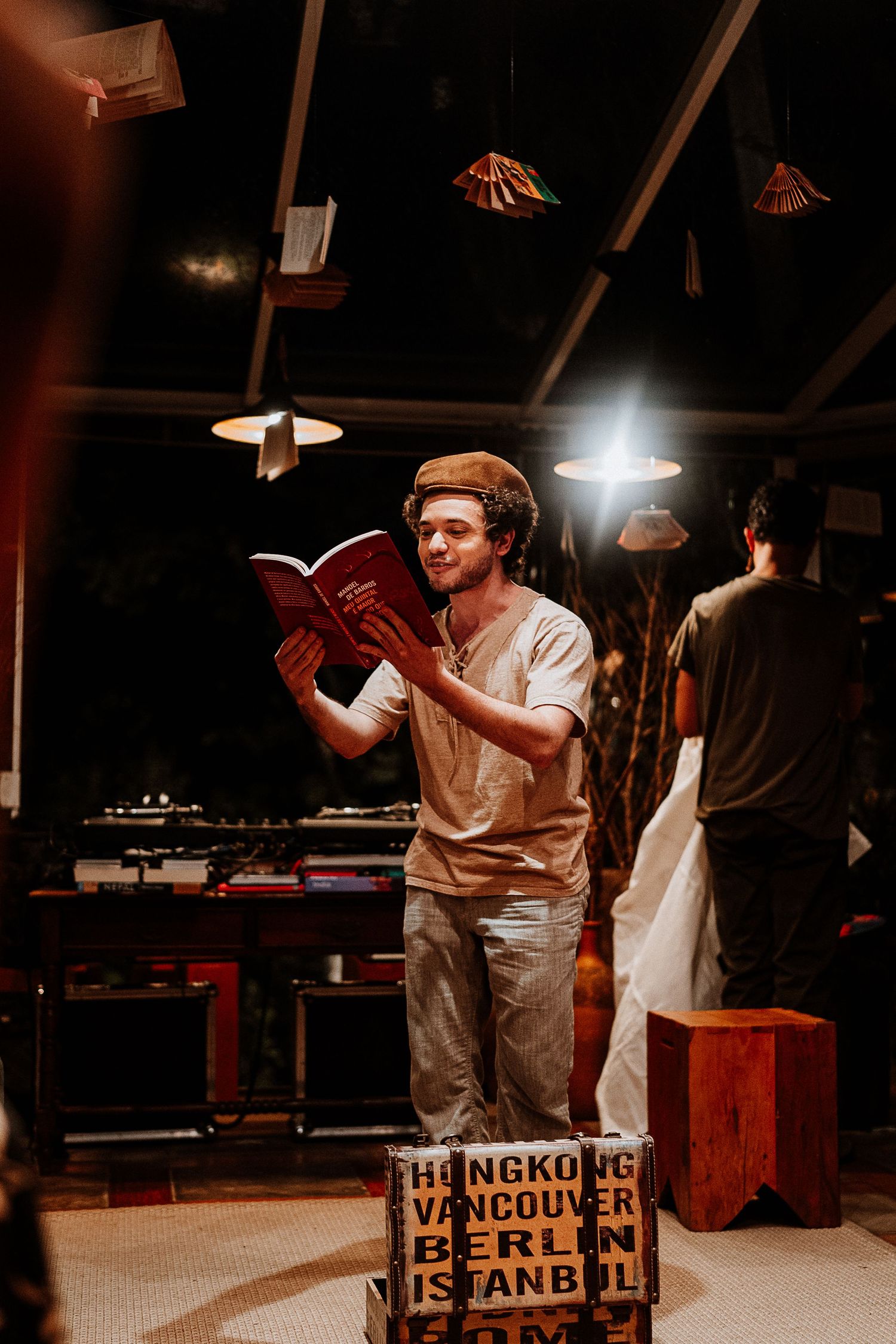 Person reading from a book while standing on a wooden crate under dim lighting.