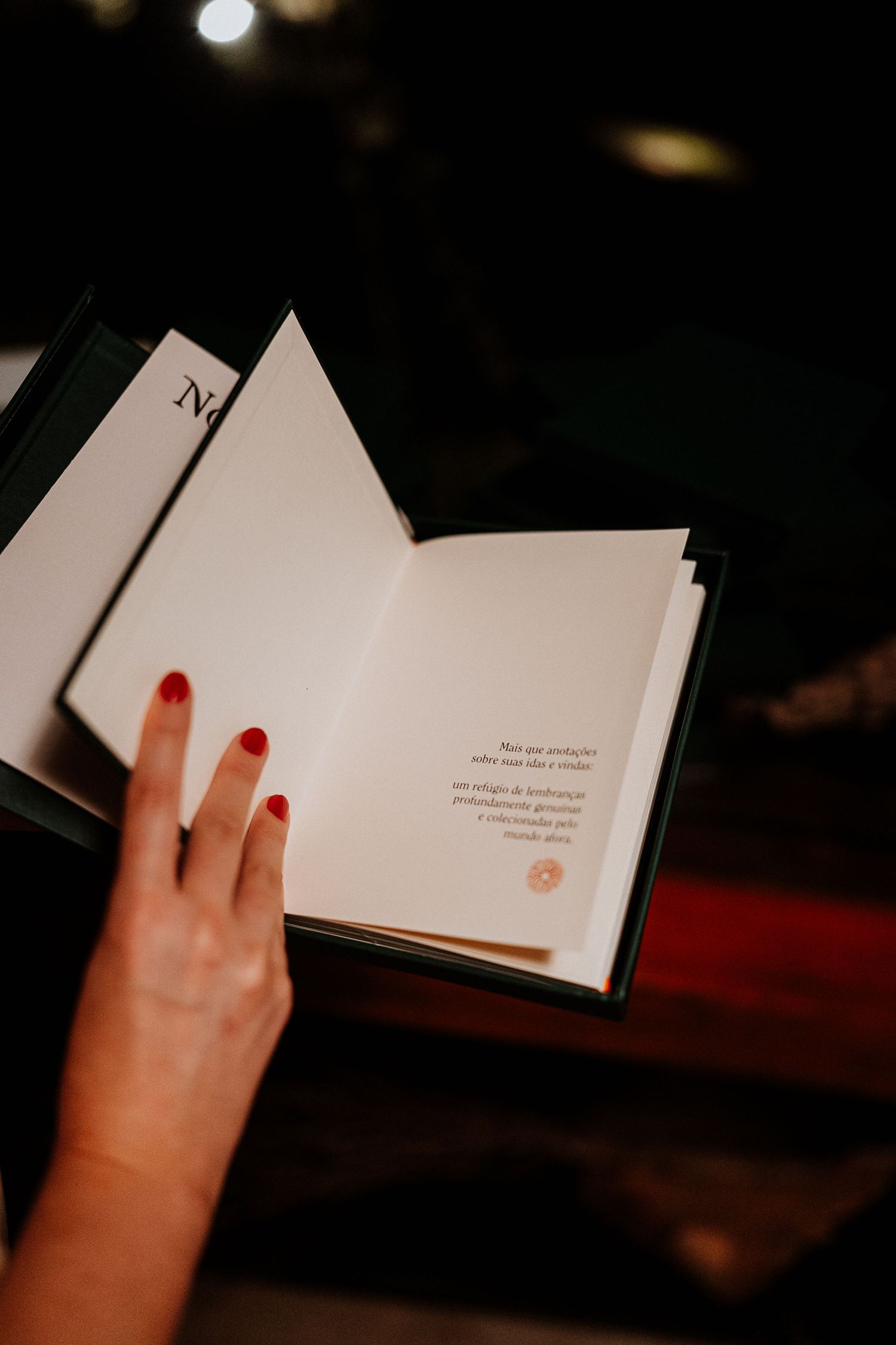 Hand with red nail polish holding open a book showing text on white pages.