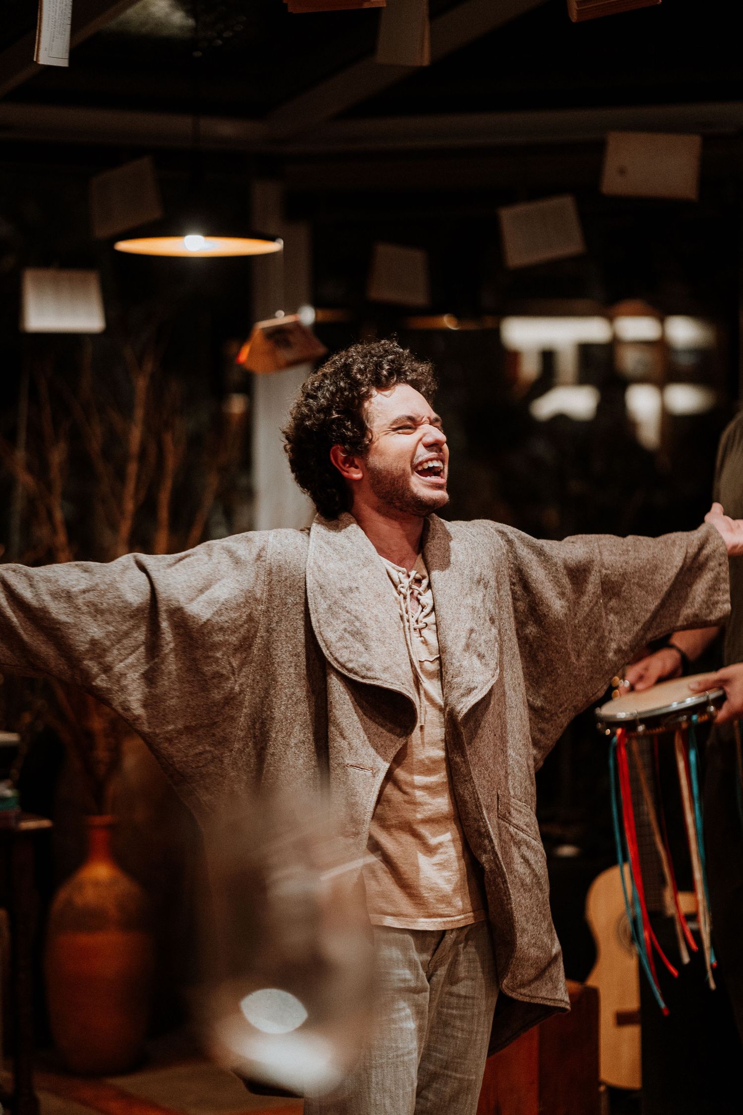 Performer in beige outfit expressing dramatic emotion during a theatrical moment.