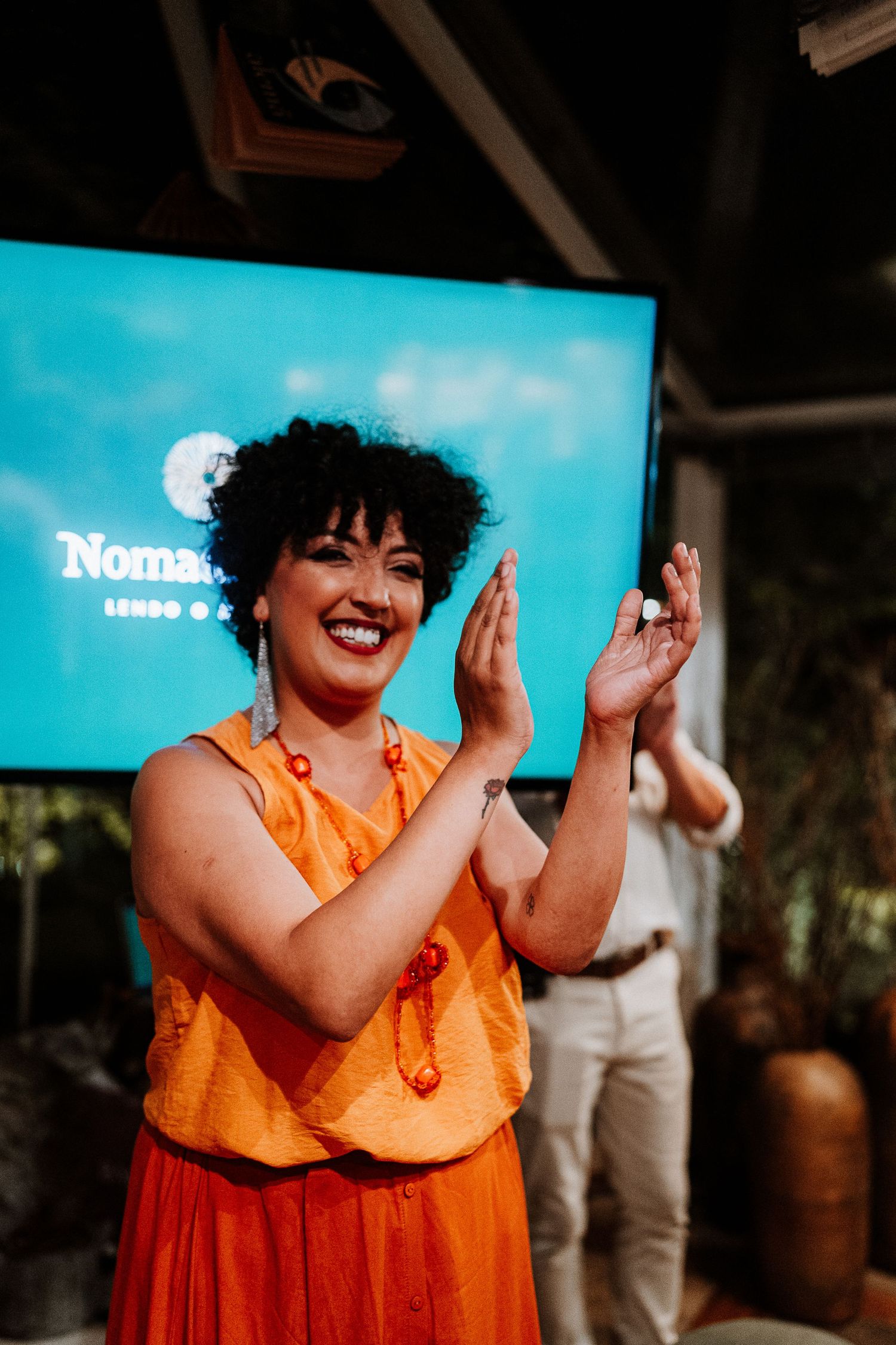 Person in orange and red outfit clapping enthusiastically in front of a blue screen.