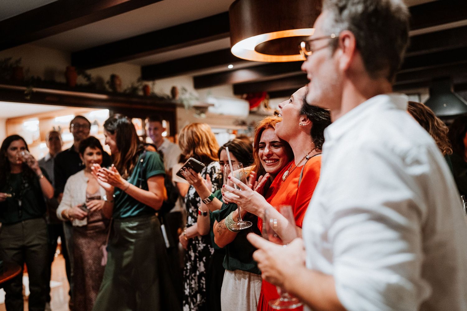 A lively celebration with people clapping and cheering at an indoor event venue with exposed beams.