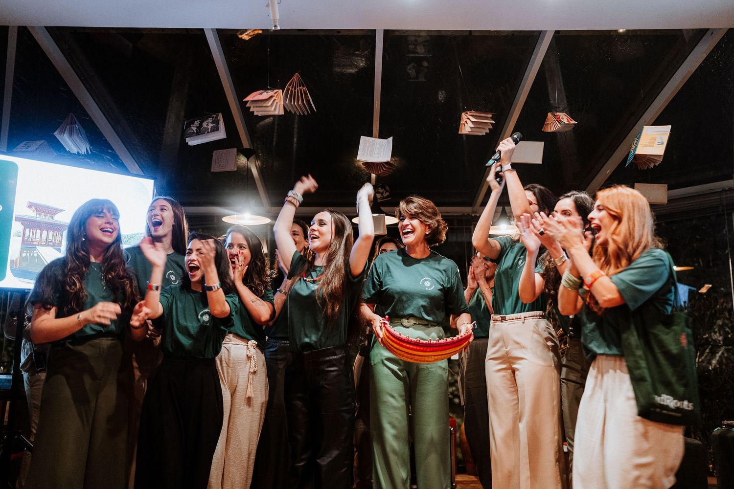 Group of people in coordinated green outfits celebrating with raised arms at an indoor venue.
