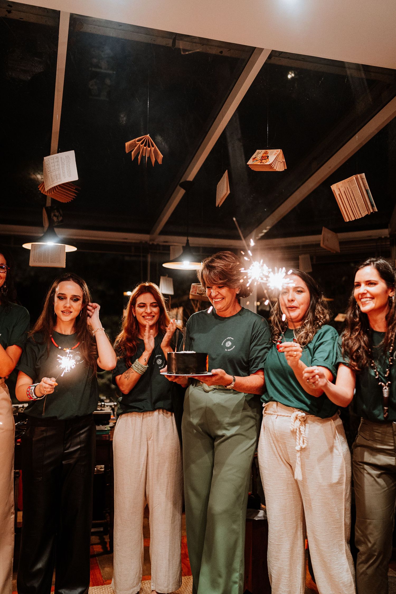 Group celebration with sparklers and cake at an indoor venue with hanging decorations.