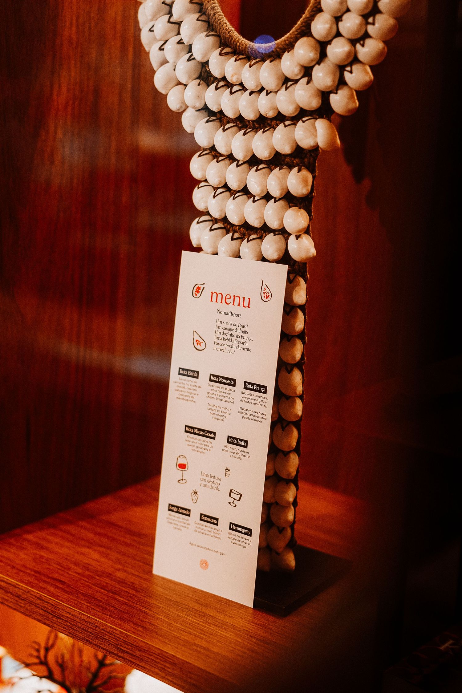Restaurant menu displayed against decorative beaded wall hanging in warm lighting.