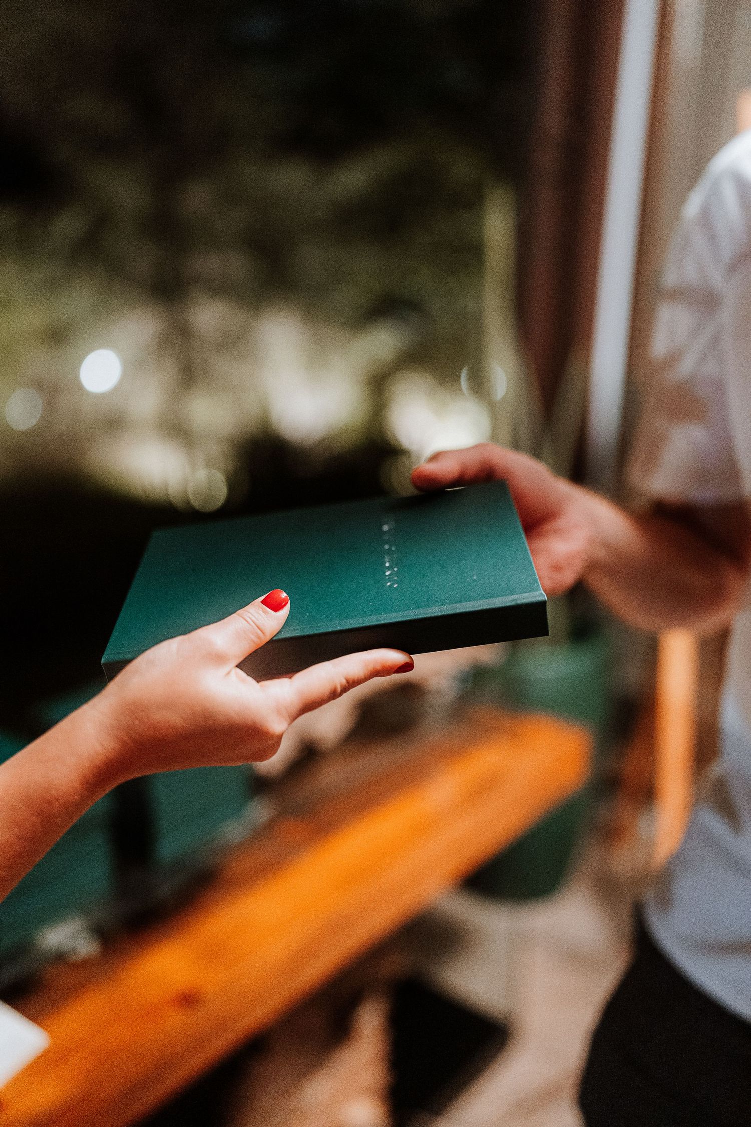 Hands exchanging a dark green book or document in atmospheric lighting.