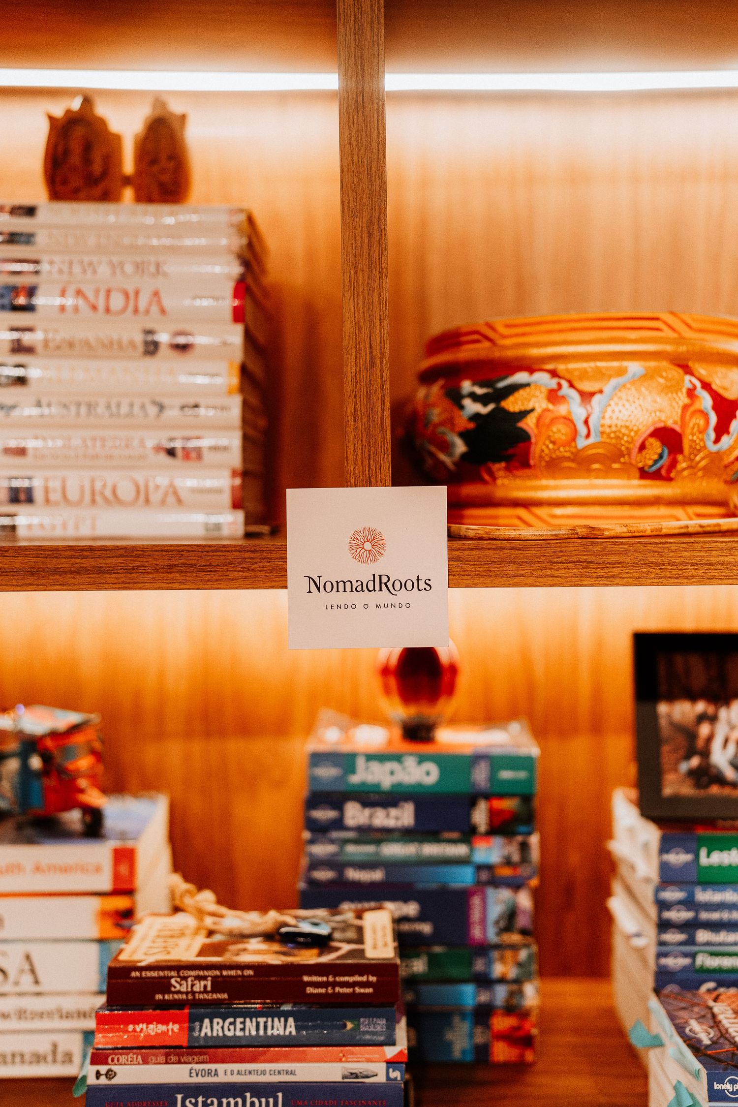 Travel books and souvenirs displayed on wooden shelves with NomadicRoots branding.