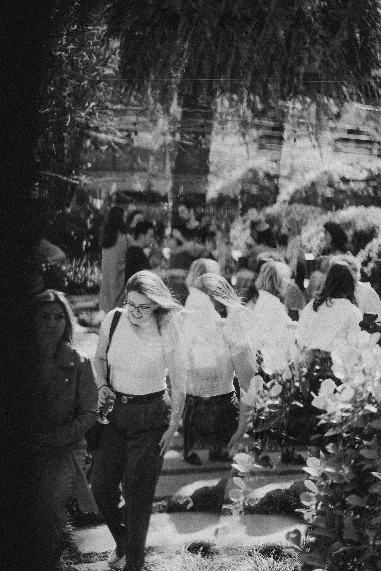 A black and white photograph of people gathering outdoors near lush greenery.