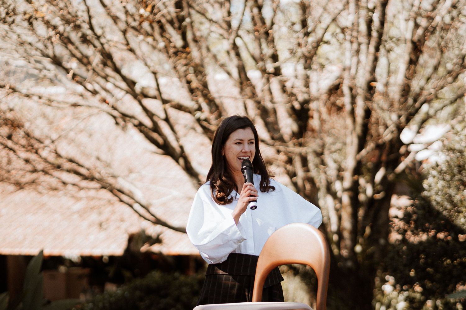 An outdoor speaking event with autumn trees in the background.