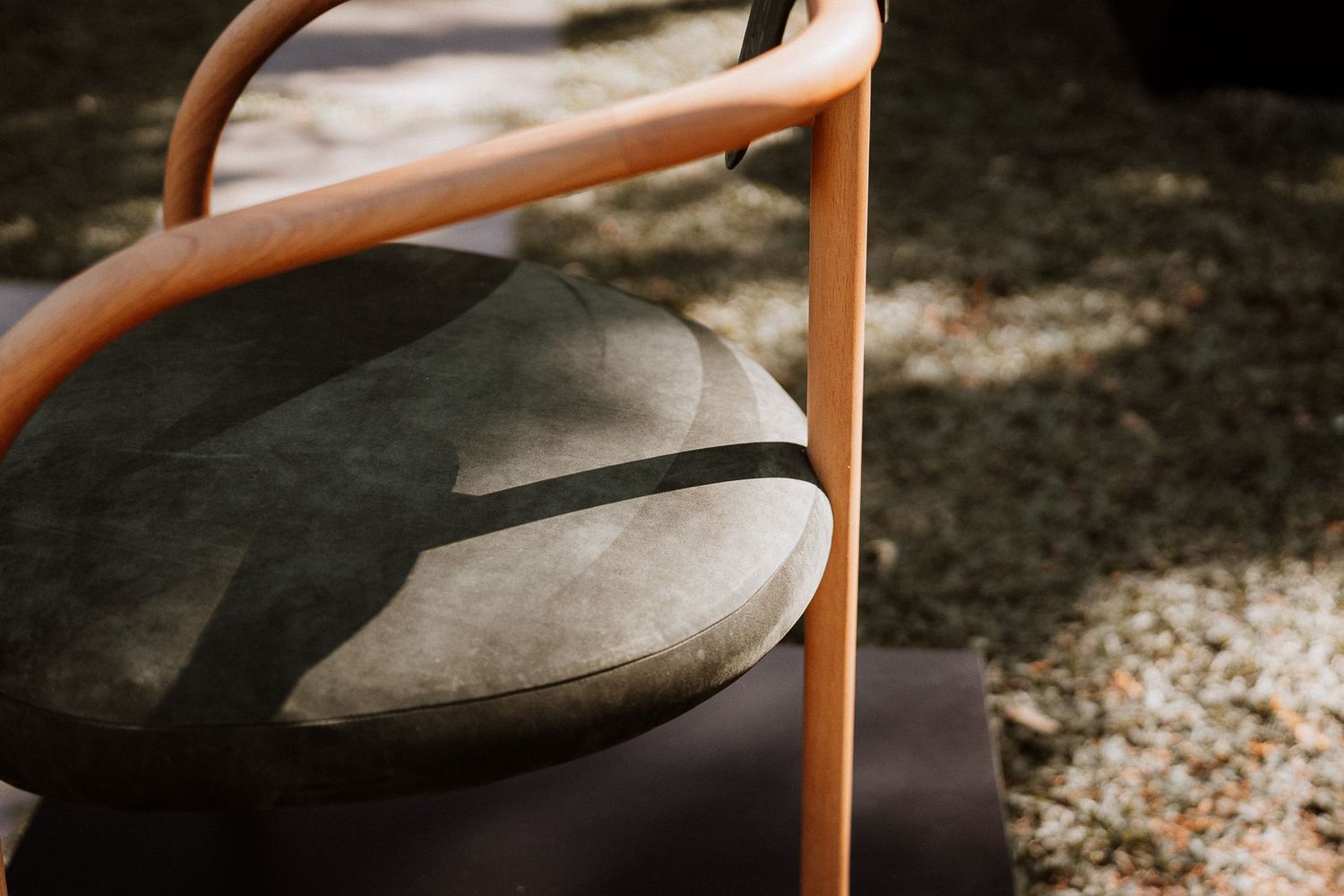 Close-up of a modern chair design showing curved wooden frame and gray cushion in sunlight.