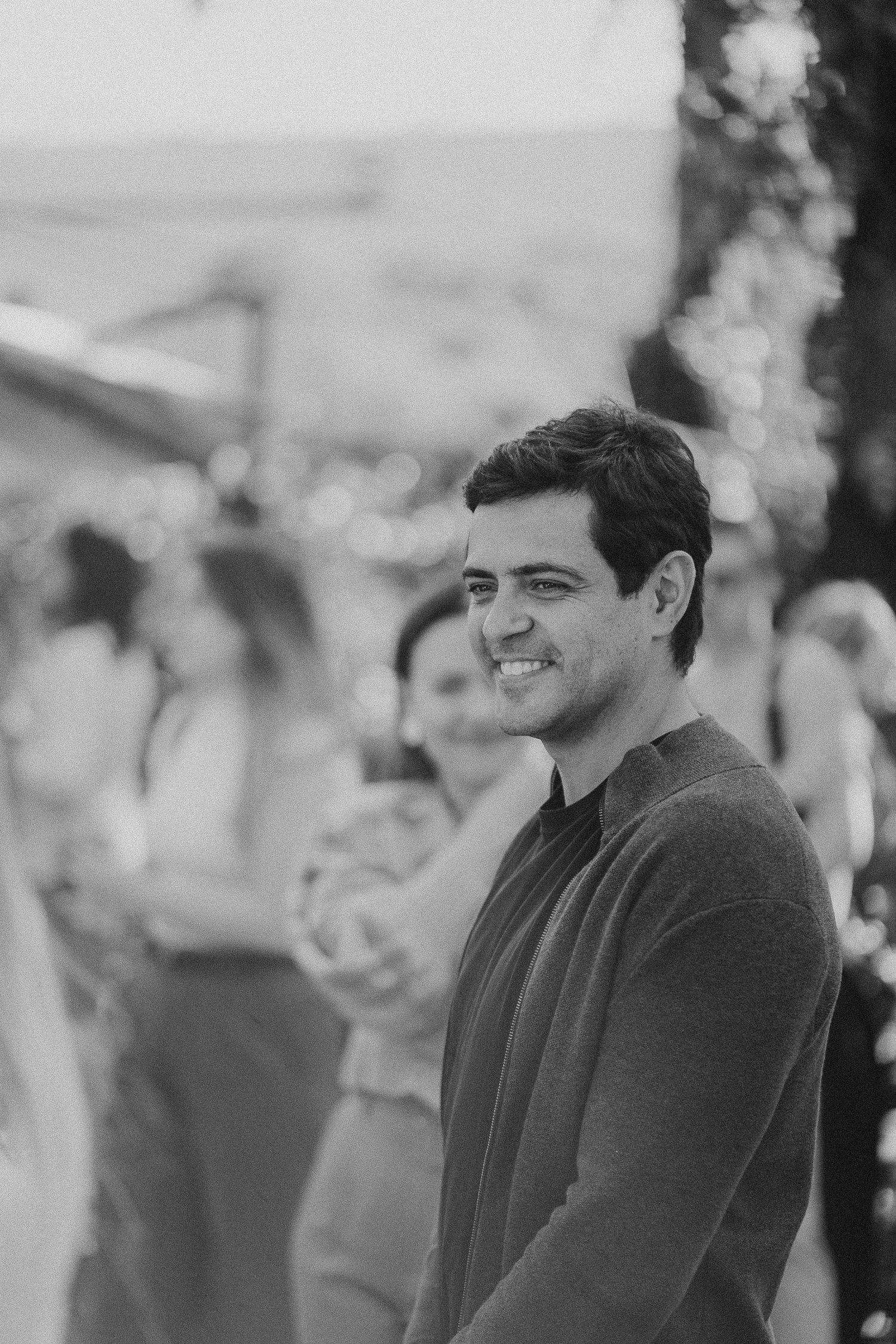 Person in dark sweater smiling at outdoor gathering in black and white photography.