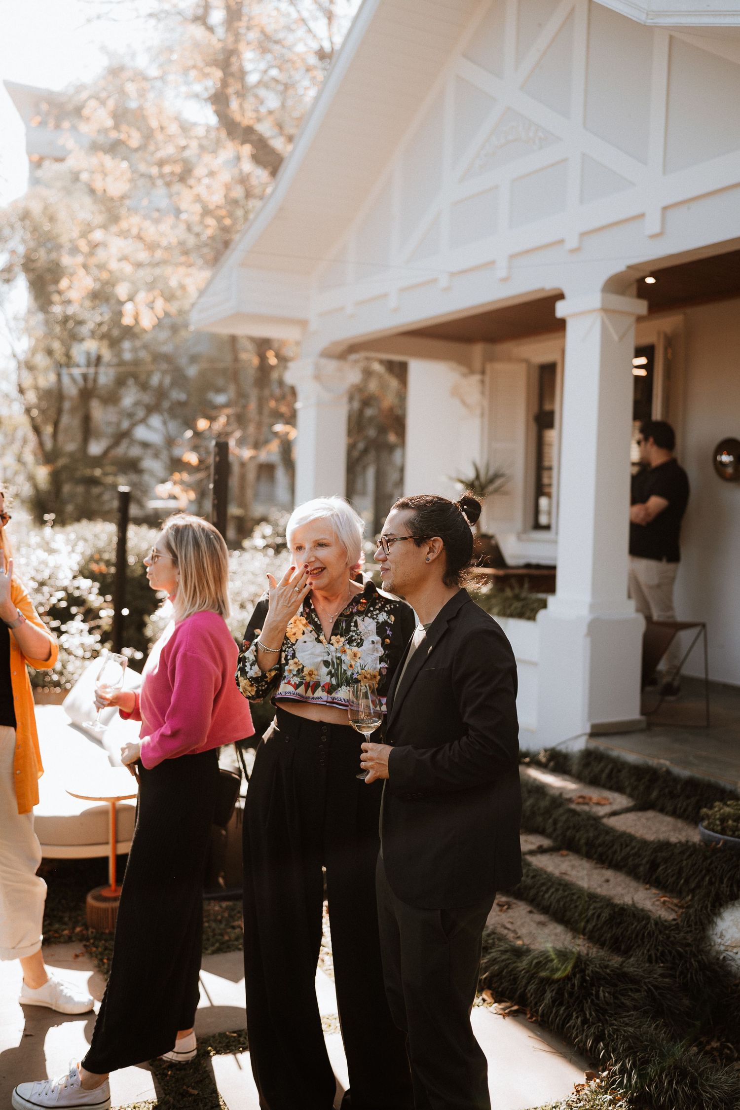 People gathered outside a white craftsman-style house during a social event.