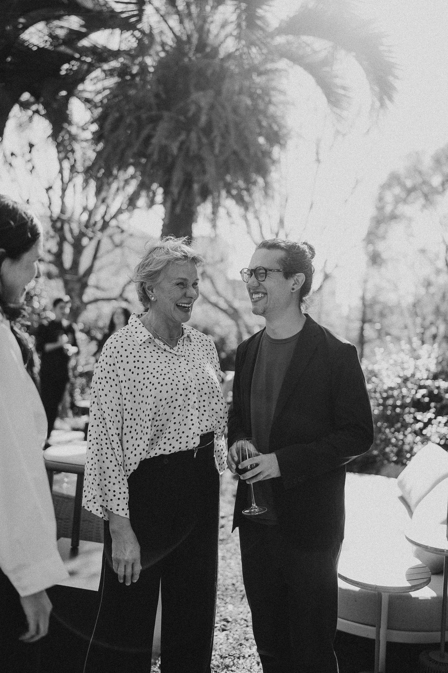Two people sharing a laugh at outdoor social gathering in black and white photography.