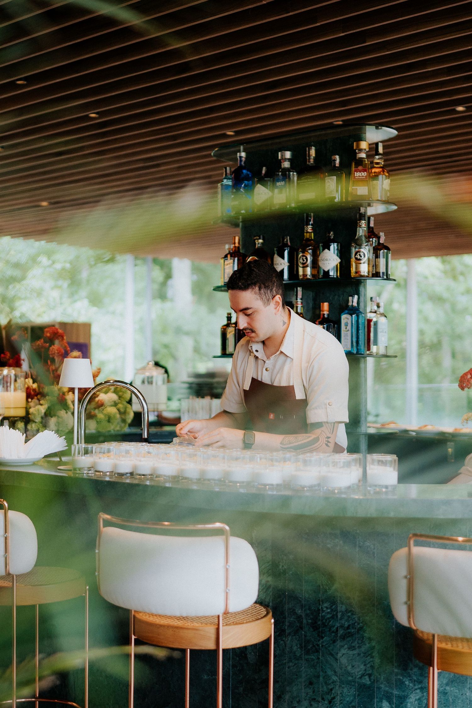 Bartender in white shirt and apron working behind modern bar counter with elegant white bar stools.