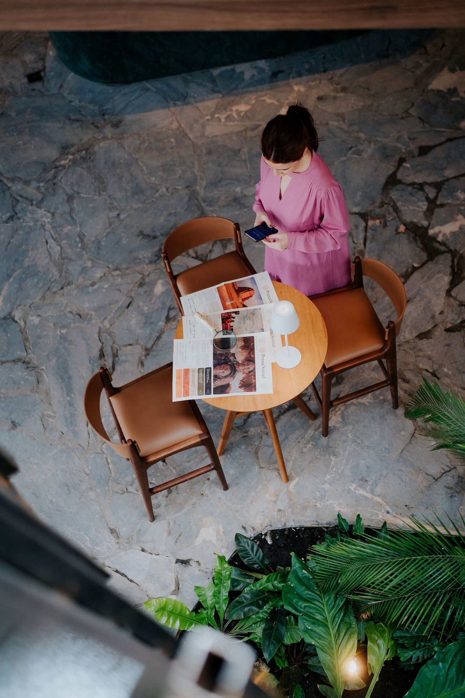 Overhead view of person in pink dress sitting at round wooden table with reading materials.