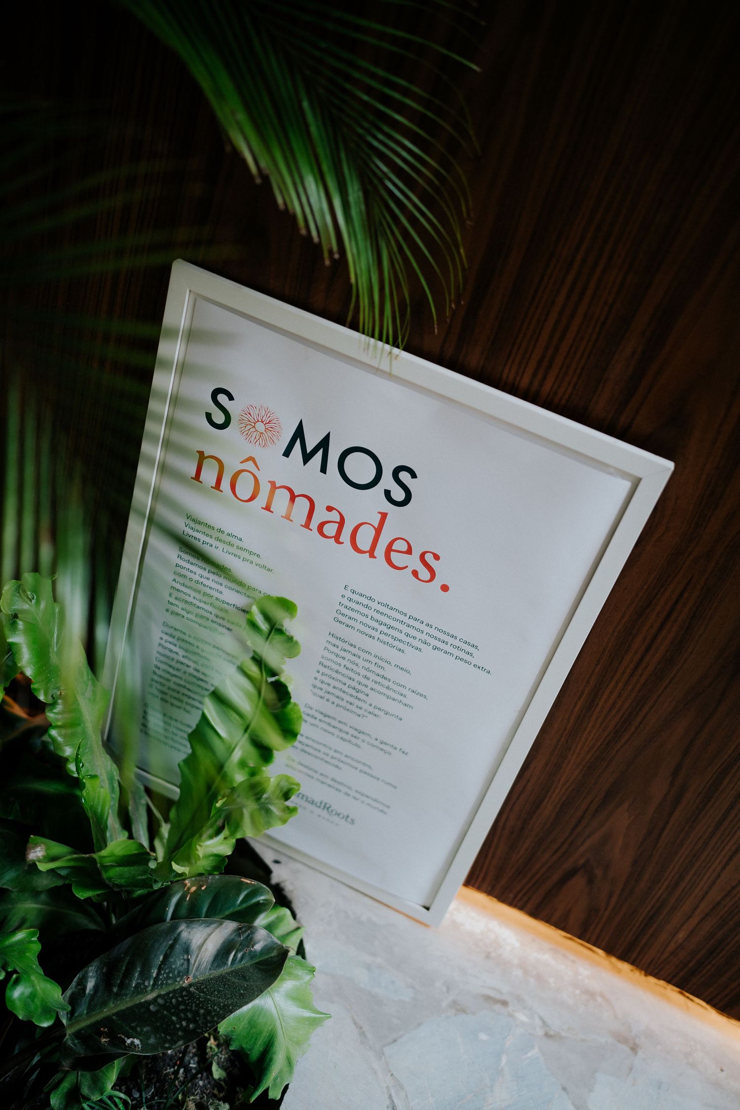 Somos Nomades sign displayed against wooden wall with tropical palm leaves.