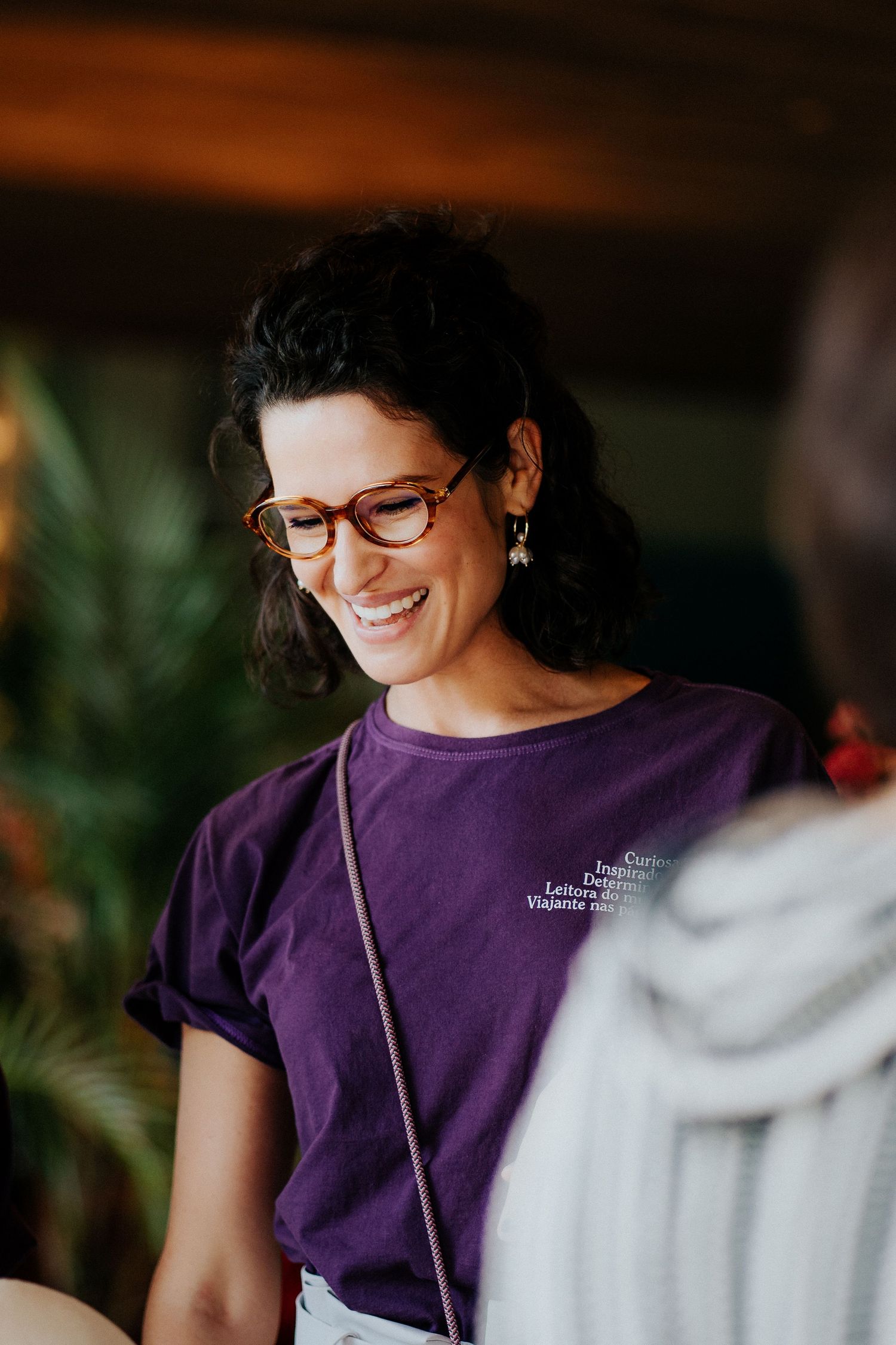 Someone wearing glasses and a purple t-shirt smiles warmly during a casual gathering.