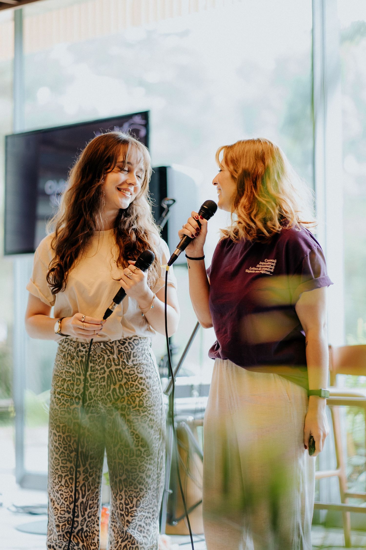 Two performers sharing a joyful moment while singing into microphones on stage.