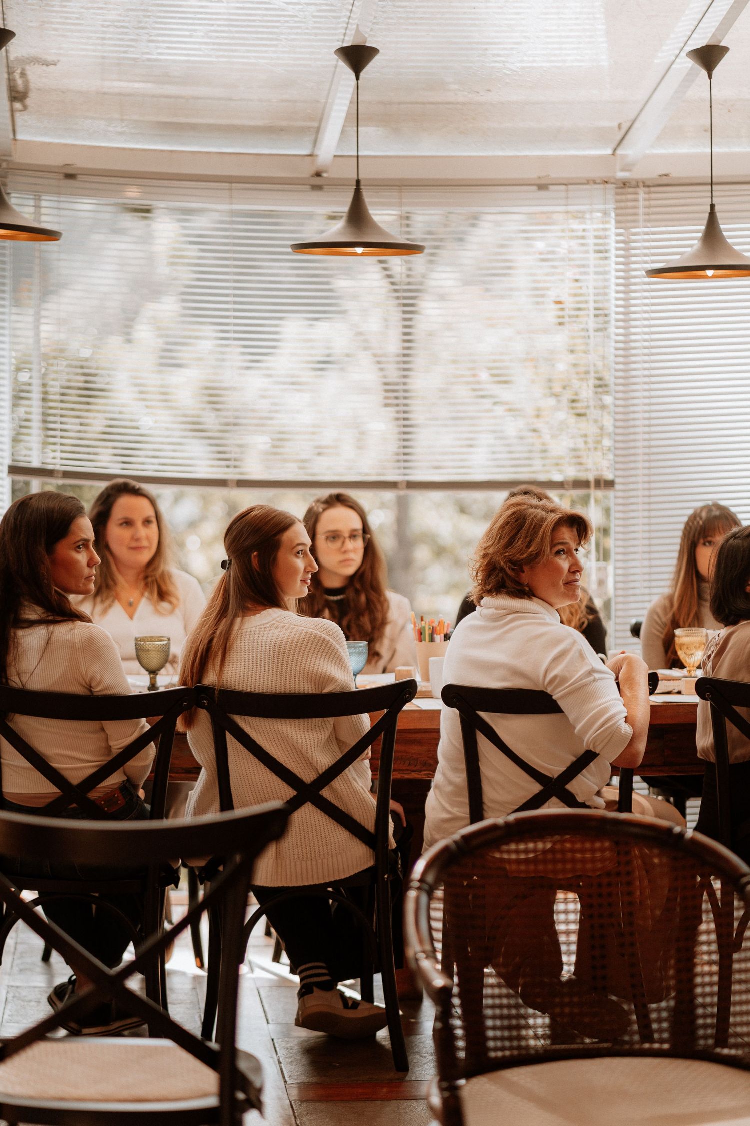 People seated at wooden chairs in a bright cafe with window light streaming in.