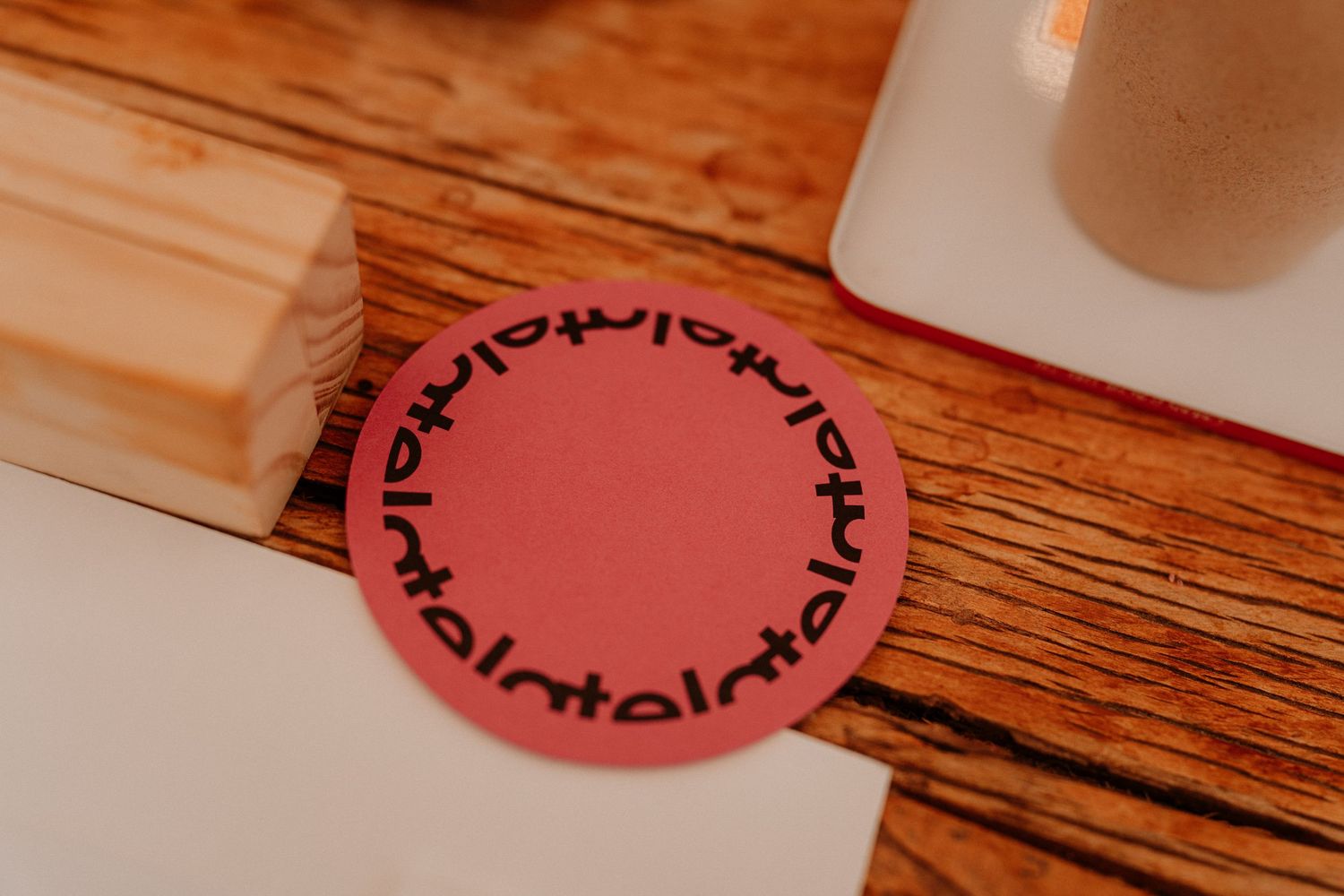 Close-up of pink circular coaster with decorative pattern on wooden table.
