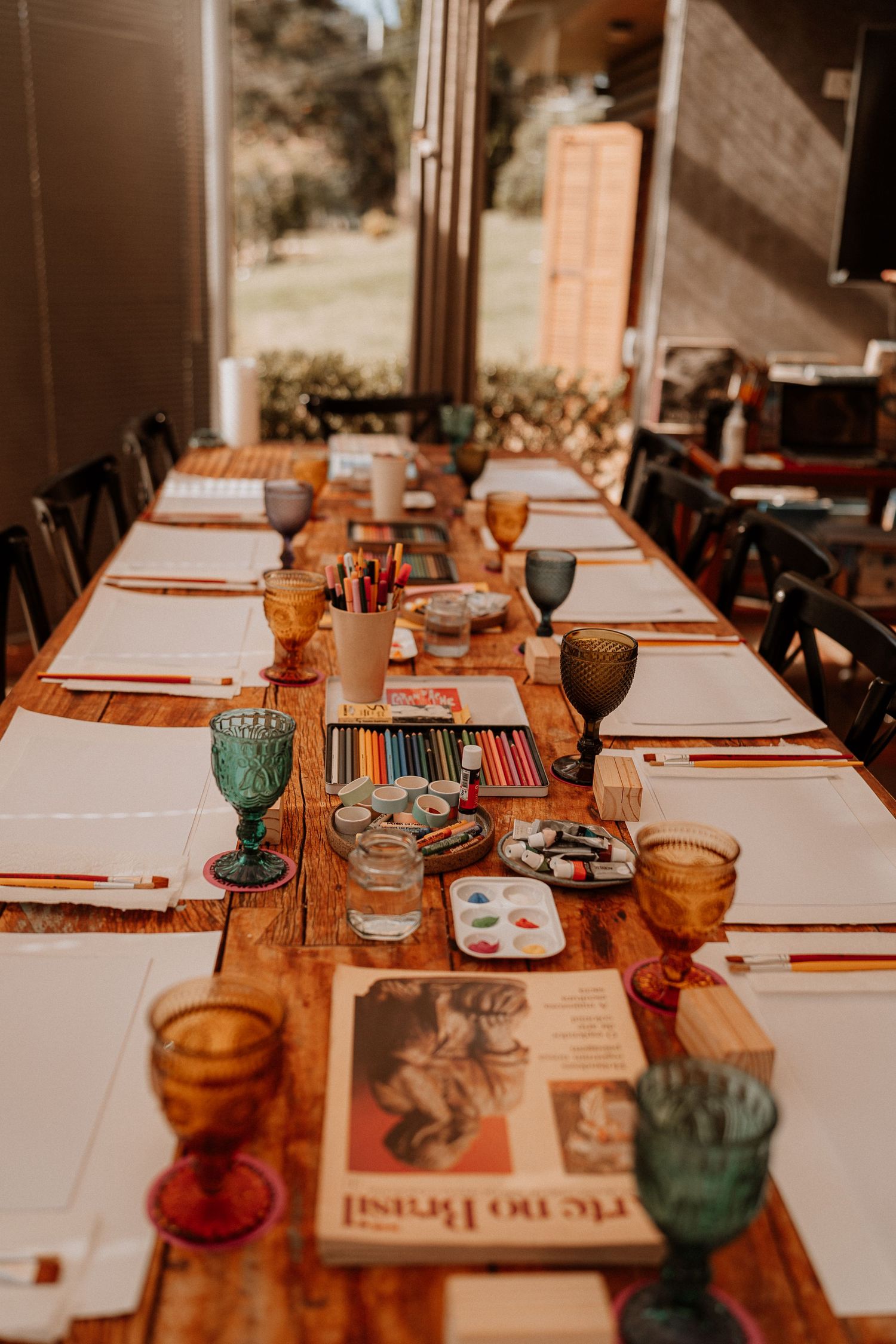 Long dining table set with colorful glasses and place settings in natural light.