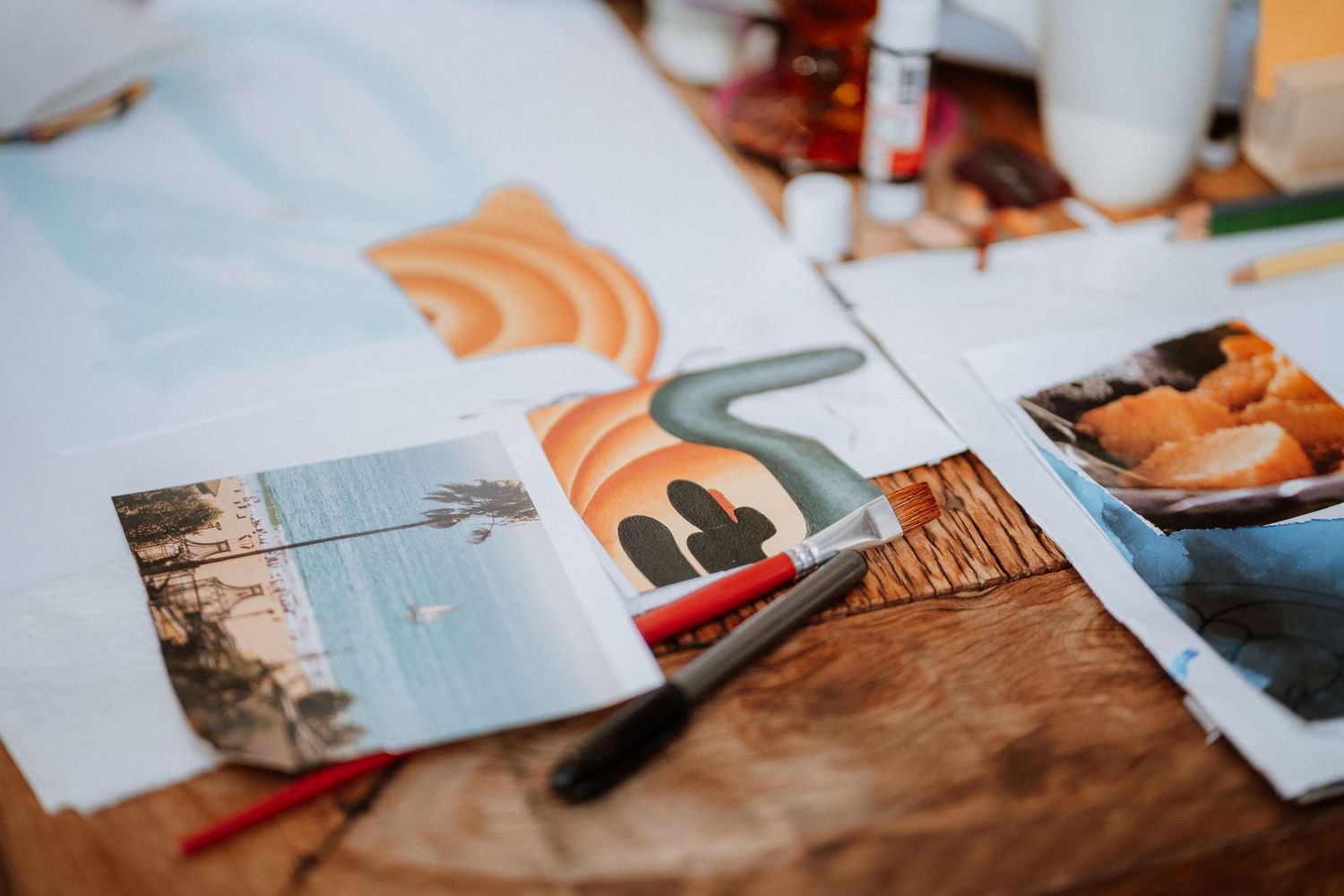 Art supplies and papers scattered on a wooden surface in natural lighting.
