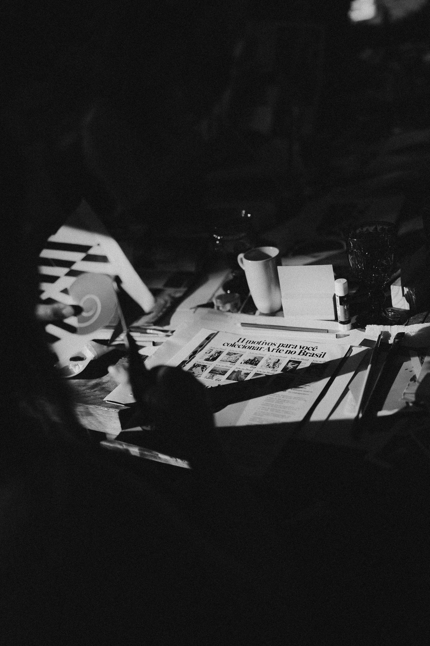 Black and white image of documents and papers scattered on a desk in dramatic lighting.