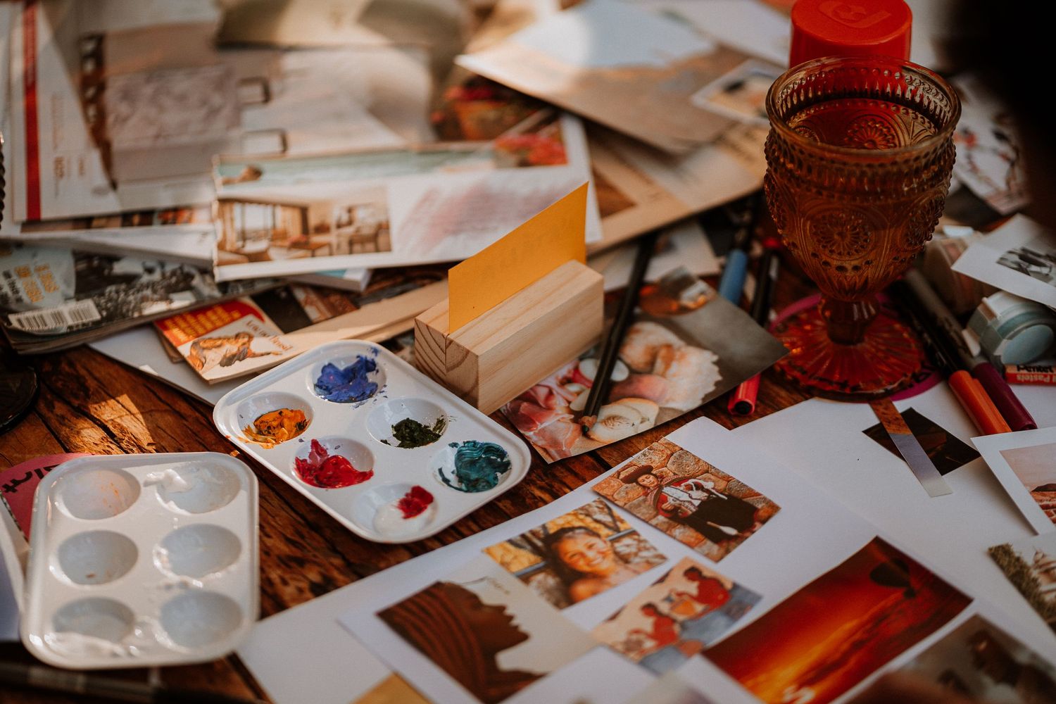 Paint palettes and photographs scattered on wooden surface with warm lighting.